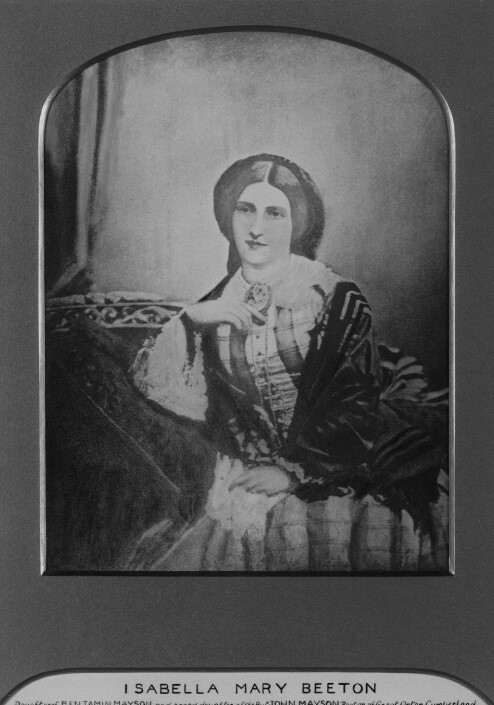 Photograph of Isabella Beeton, 1857.  Isabella wears a plaid dress and a dark shawl.  She is seated and rests her elbow on a cushion.